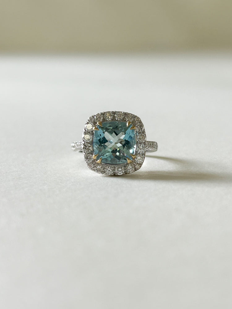 A beautiful cushion cut aquamarine and diamond cluster ring, set into white gold, with yellow gold claws over the aquamarine.