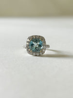 A beautiful cushion cut aquamarine and diamond cluster ring, set into white gold, with yellow gold claws over the aquamarine.