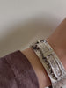 Video of bangle on model's wrist, brown shirt sleeve visible.